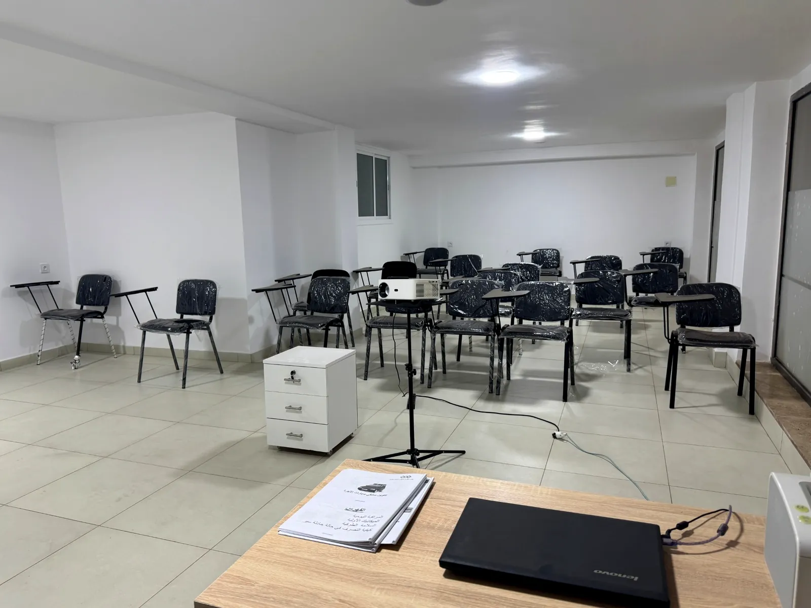 La salle de cours avec ses chaises à tablette, le vidéoprojecteur et le support de cours sur le bureau